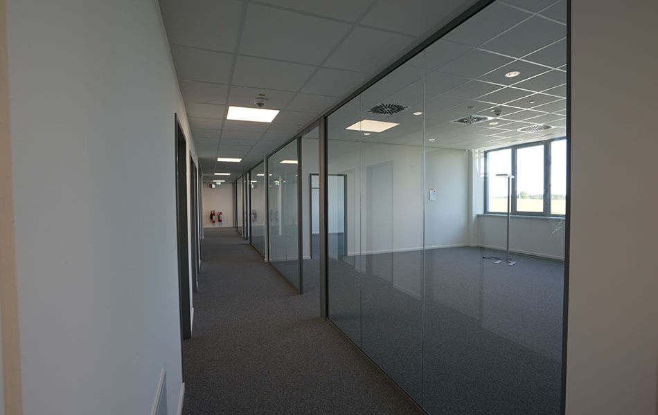 [Translate to Chinese:] Heller Büroflur mit Glaswänden und Teppichboden, Blick in noch unmöblierte Büros.